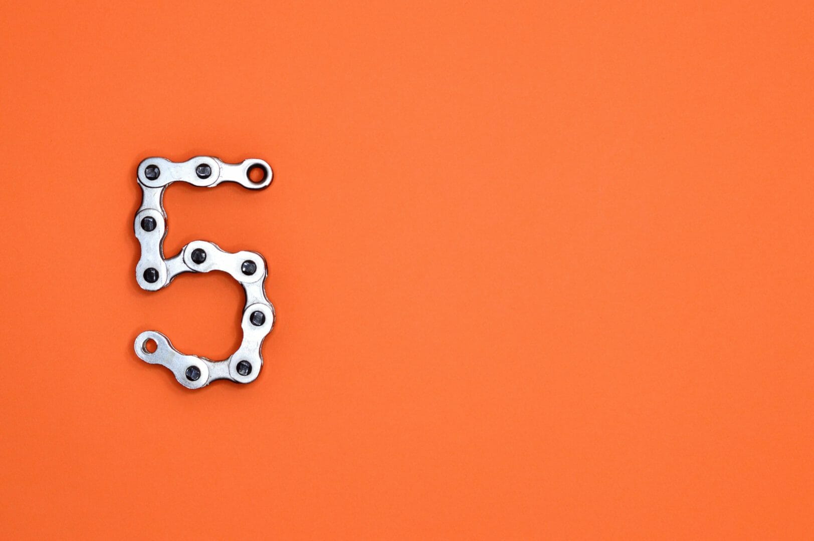 Bicycle chain arranged in the shape of the number 5 on an orange background