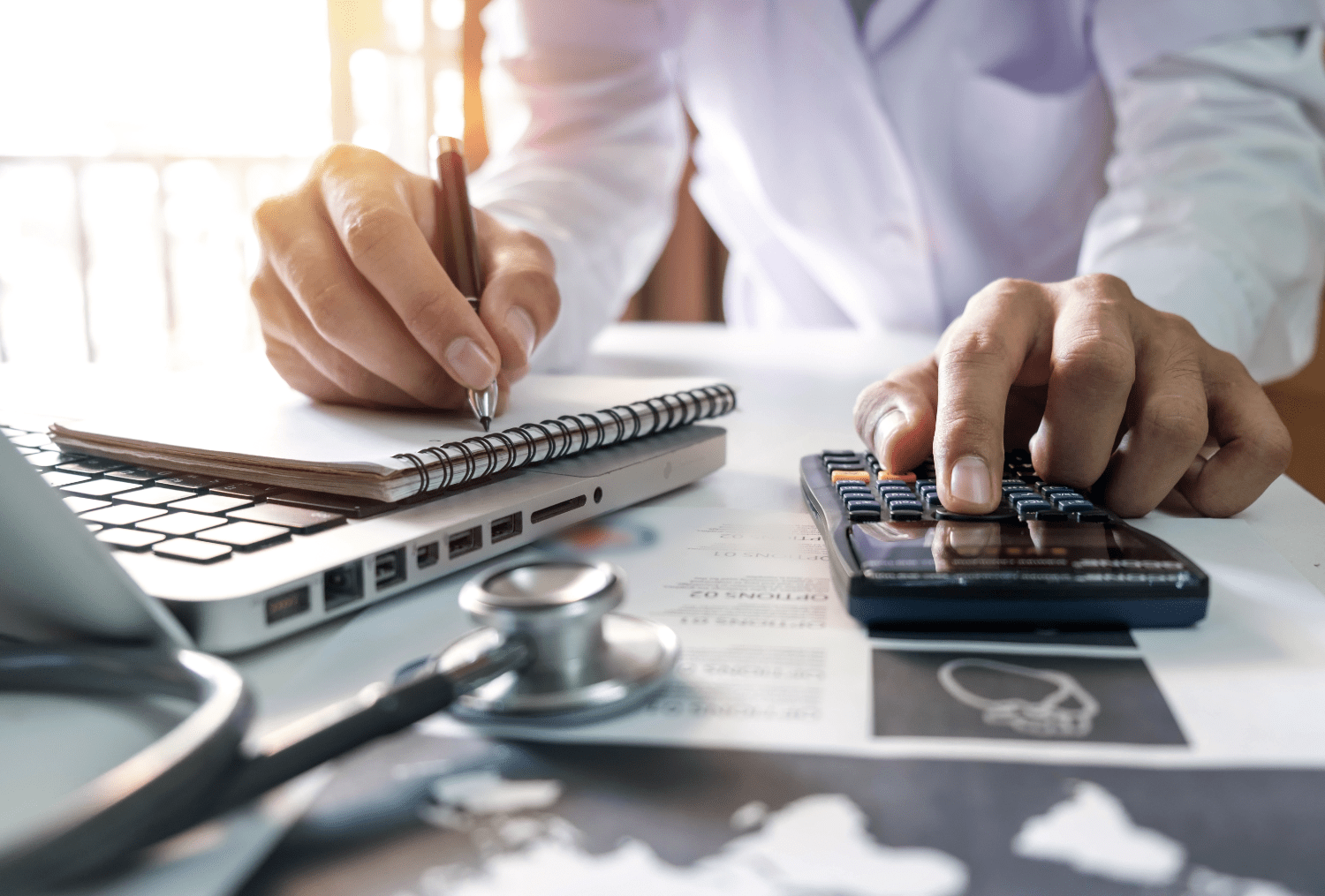 Person using a calculator with a notepad and stethoscope on the desk and the 'foxhire' logo in the foreground