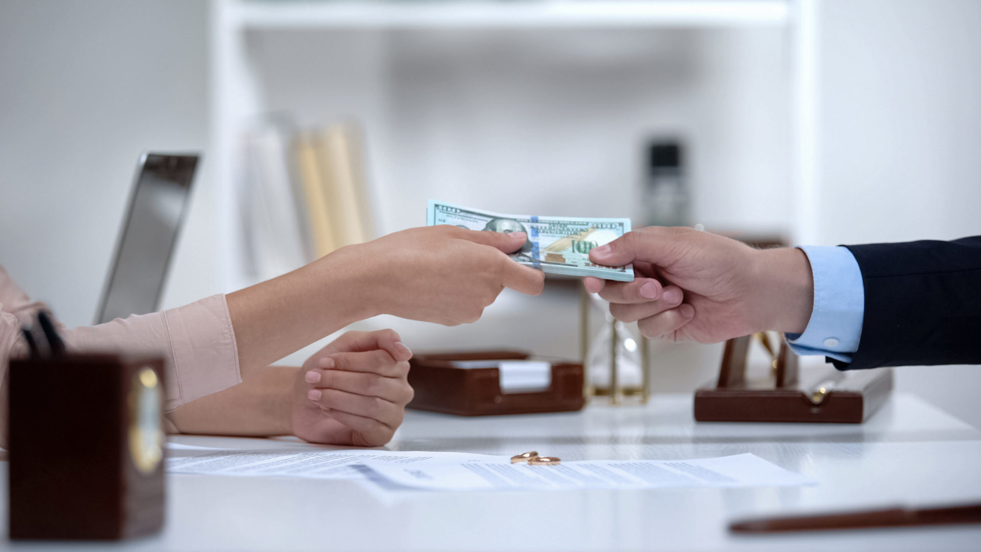 Close-up of two people exchanging money across a table with documents and pen