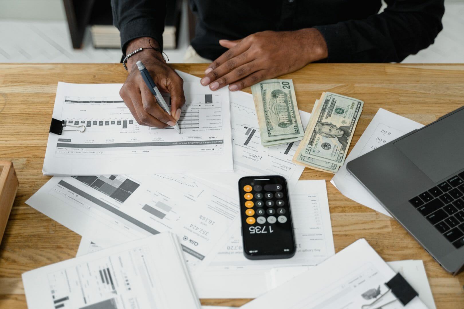 Person working at a desk with documents, a calculator, and cash