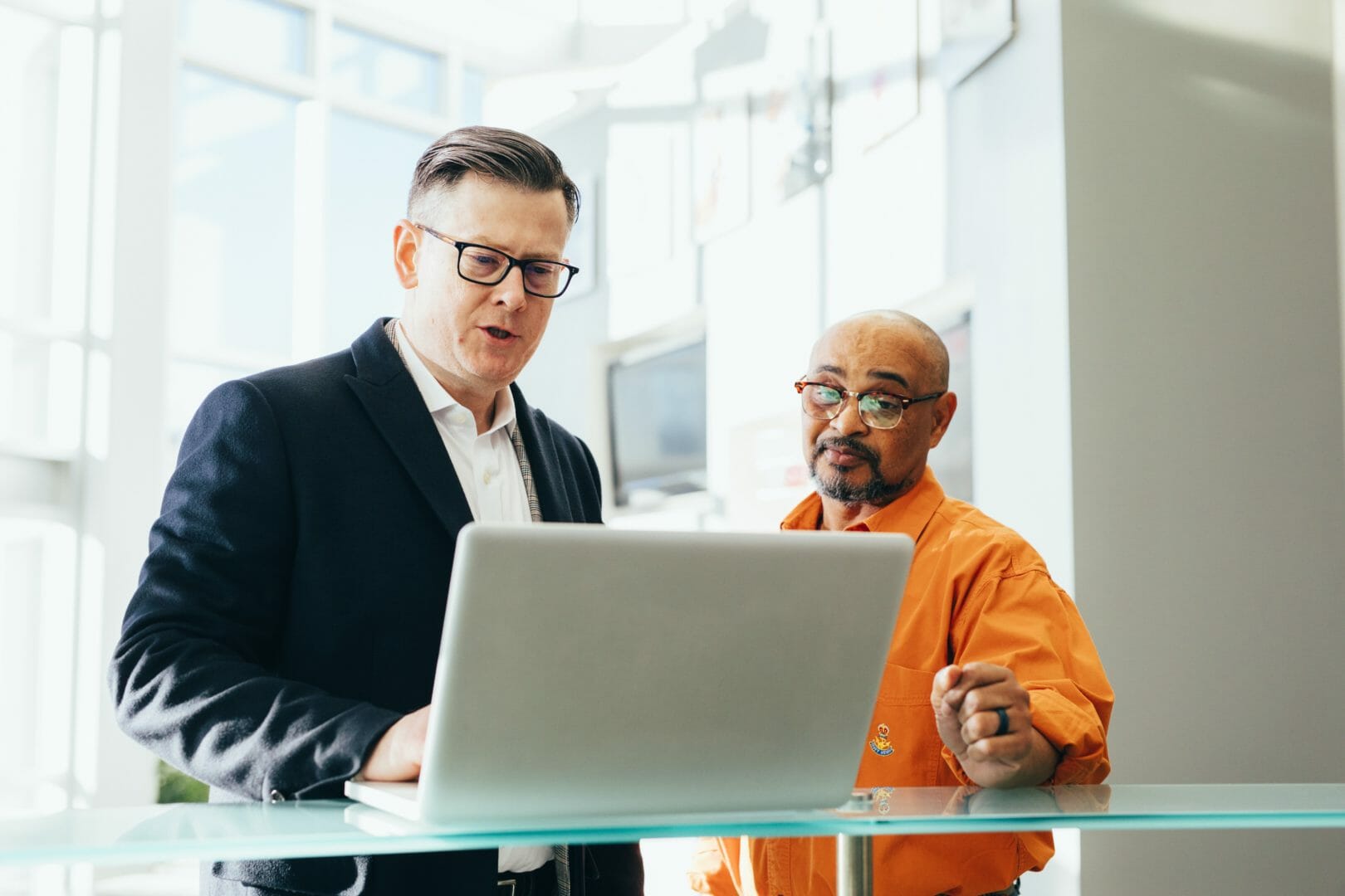 Two men in a professional setting looking at a laptop together