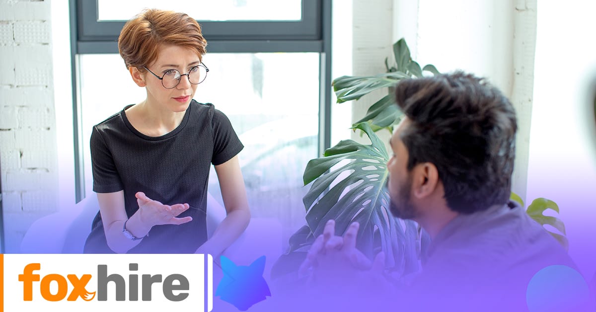 Two people engaged in a conversation in an office setting with the 'foxhire' logo in the foreground