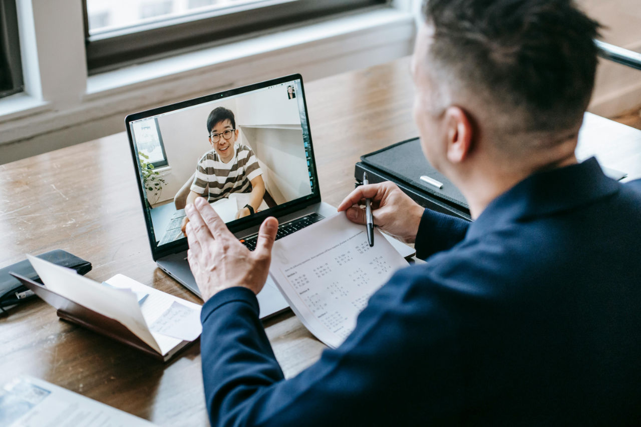 Man looking at a laptop where a guy in a striped shirt is smiling back.