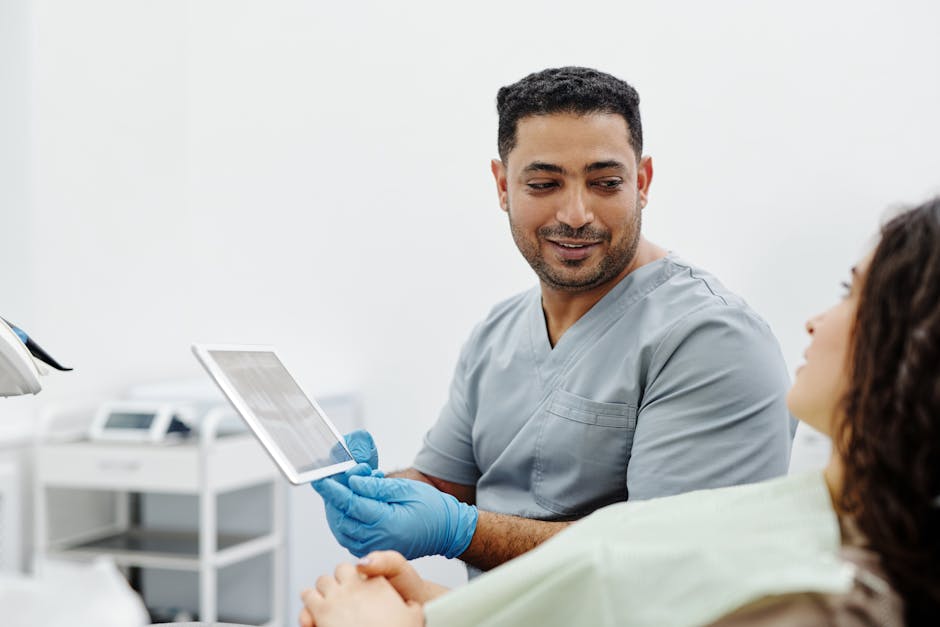 Healthcare worker in scrubs reviewing tablet records with a patient in a bright clinical setting