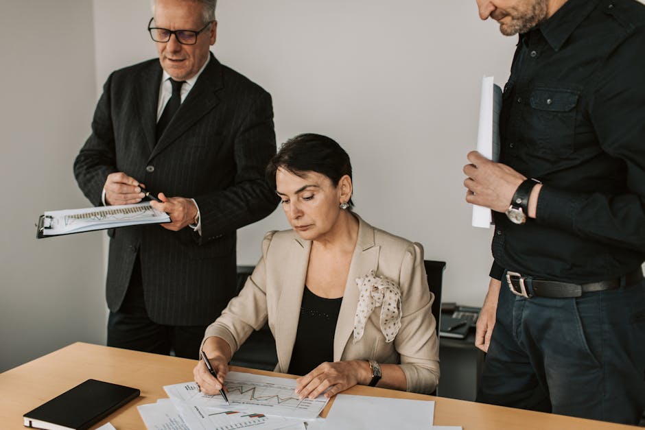 Three professionals reviewing printed business charts at an office desk during a compliance review meeting