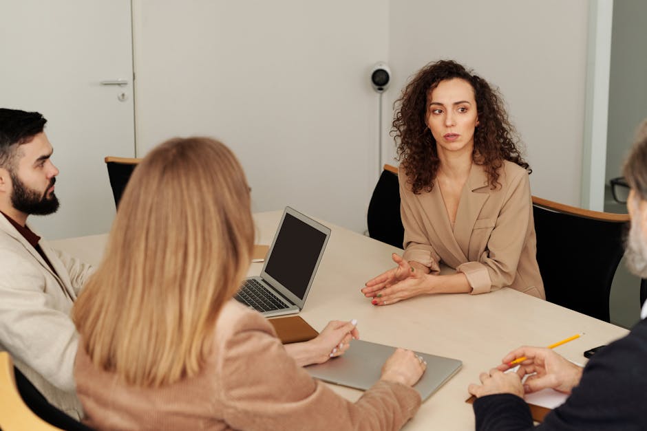 Four professionals seated around an office table with a laptop in active discussion
