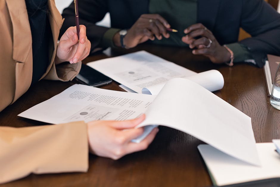 Two HR professionals at a polished wooden desk reviewing multi-page employment compliance documents with pens