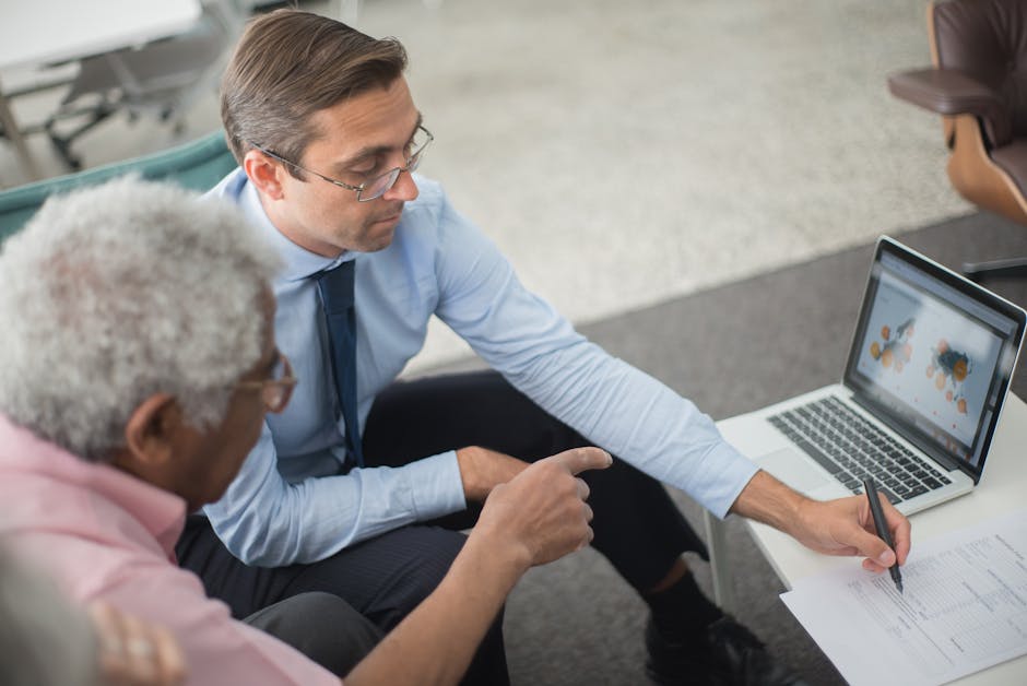 Two business professionals seated together reviewing and signing a contract document with a laptop on the table