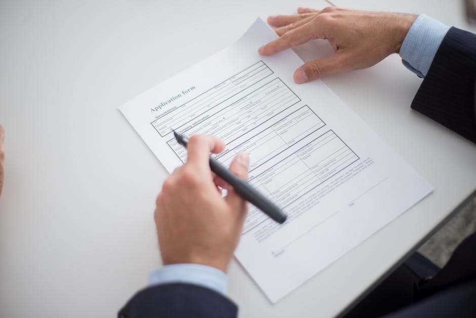 Two professionals reviewing a printed multi-section form across a desk, one holding a pen above the page