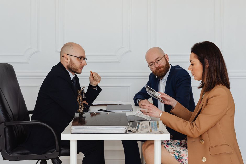 Three professionals in business attire reviewing legal documents at a white office desk