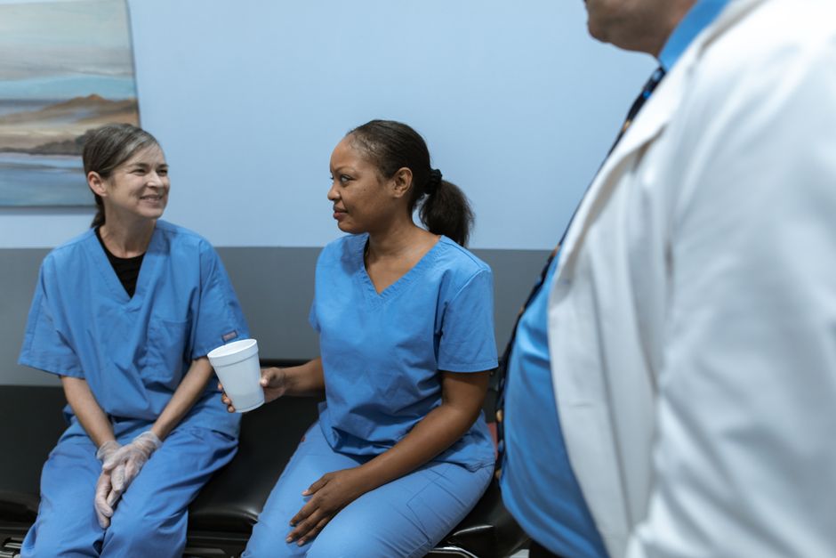 Two nurses in blue scrubs sitting together in conversation in a hospital break area