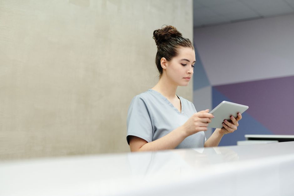 Healthcare worker in gray scrubs reviewing a tablet at a clinic reception desk