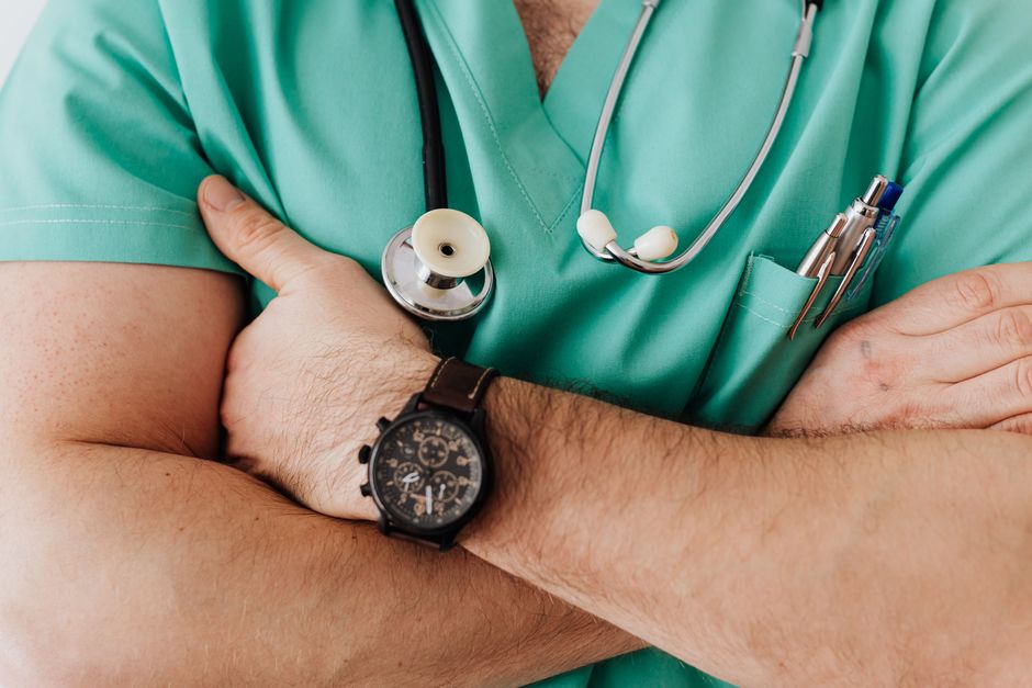 Close-up of a clinician's crossed arms in green scrubs with a stethoscope and wristwatch