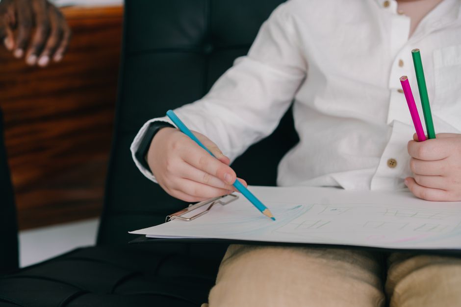 Child's hand gripping a colored pencil while drawing during a fine-motor therapy exercise