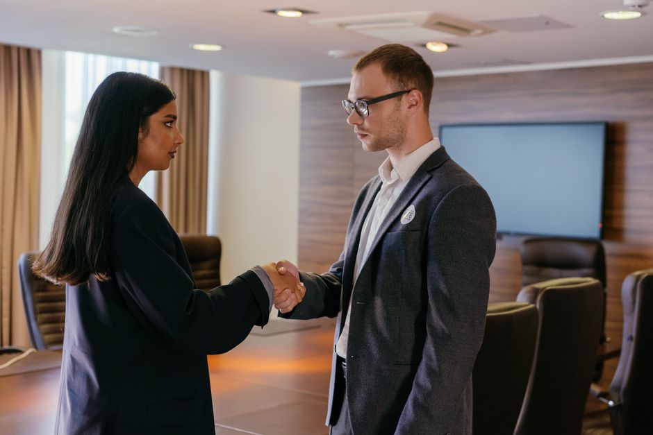 Businesswoman and businessman in suits shaking hands in a modern conference room after reaching an agreement