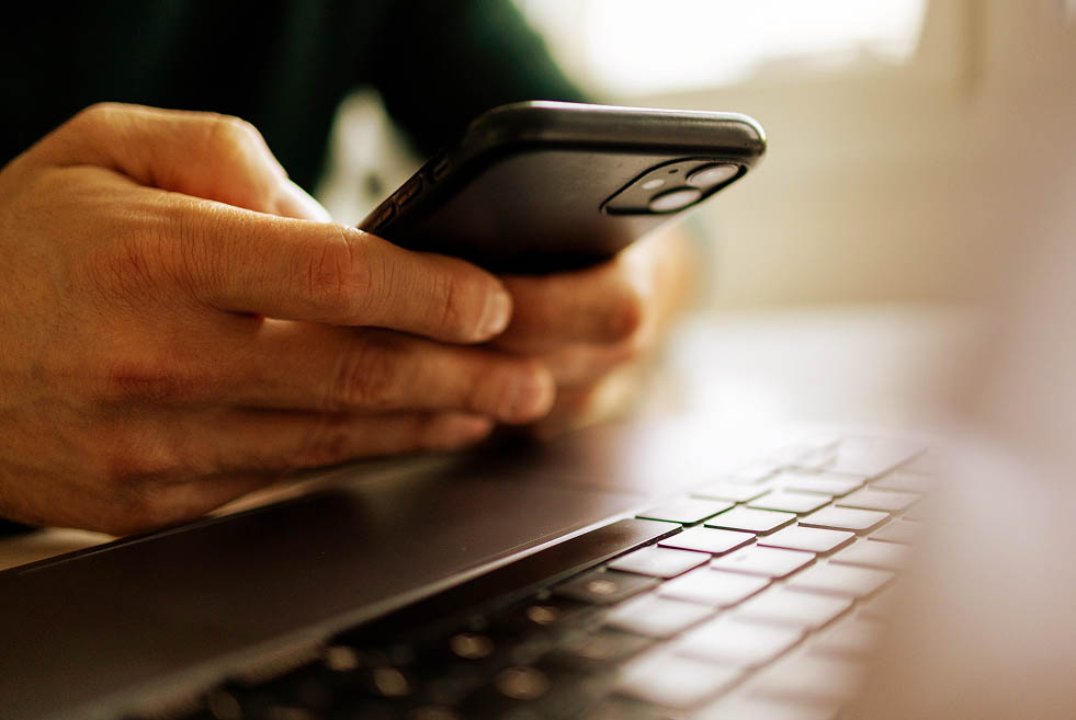 Macro shot of a person holding and typing on a mobile phone, while over a laptop