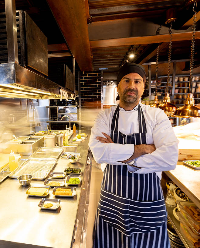 A trained chef standing in busy kitchen, staring at the viewer