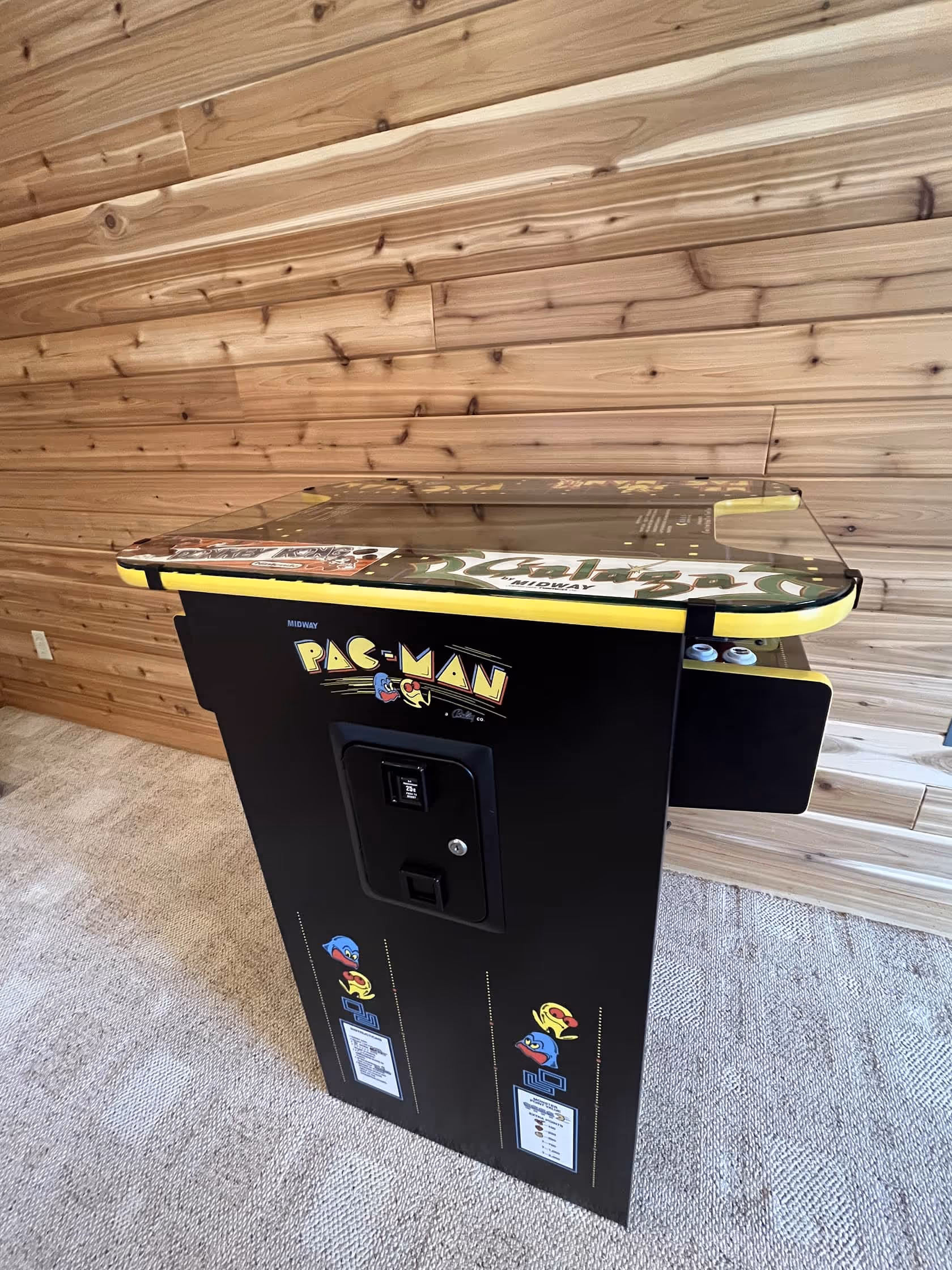 Classic Pac-Man arcade game table placed in a cozy, wood-paneled room.