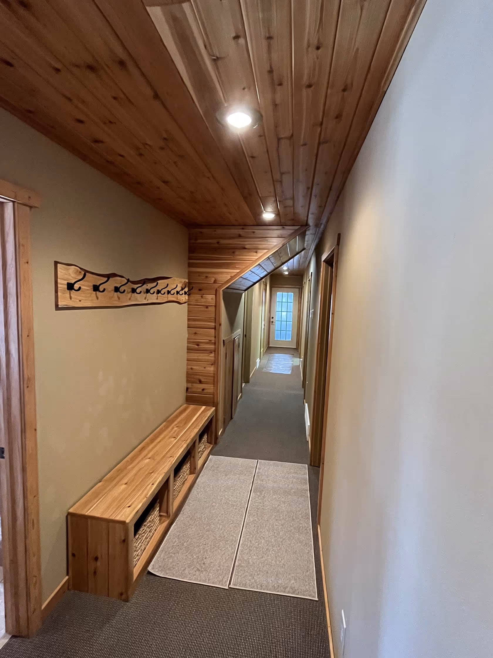 Warm, wood-paneled hallway with an entry bench and coat hooks, leading toward guest rooms at Matson Lake Lodge.