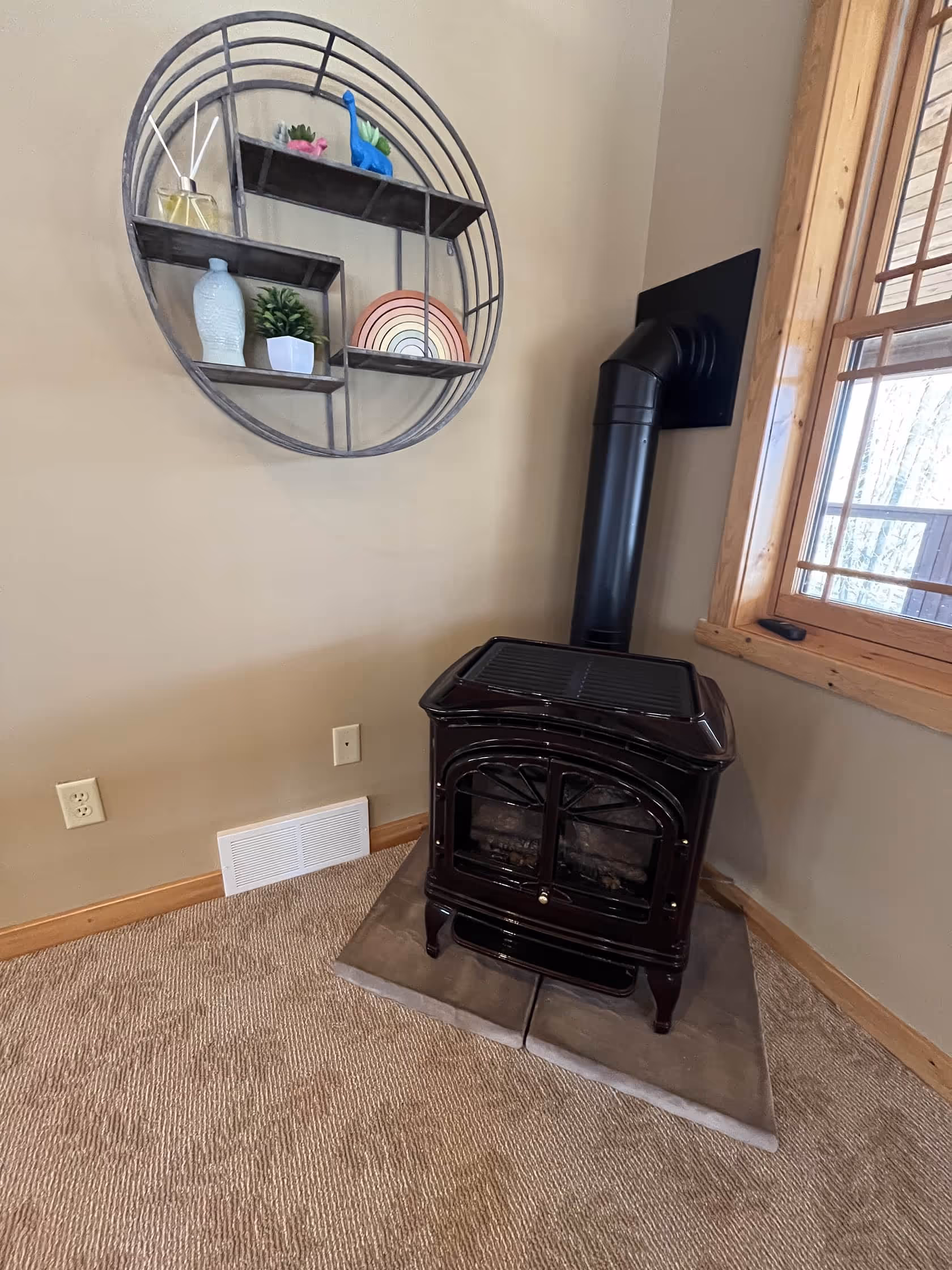 Small cast iron stove set in a cozy corner with rustic shelving and a window overlooking the outdoors.