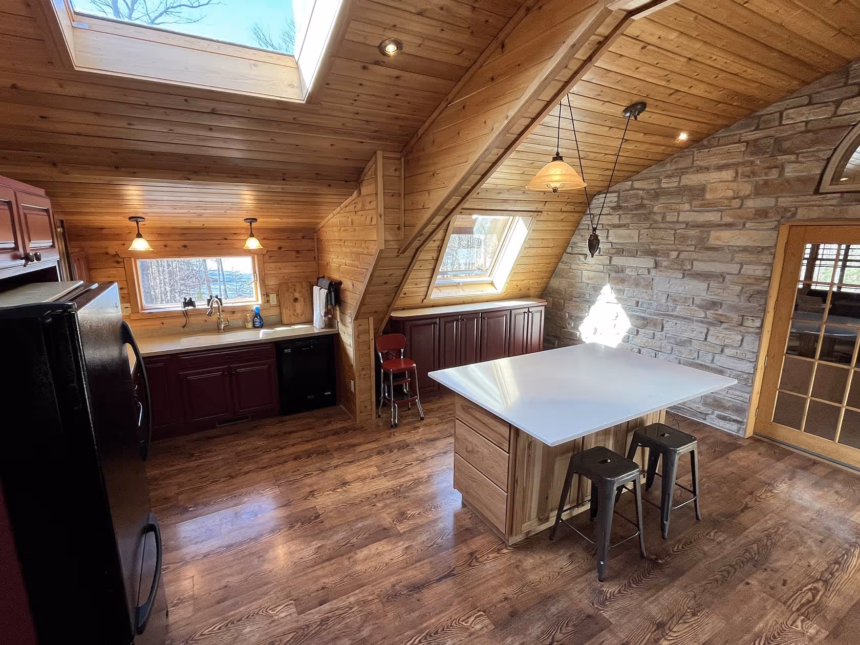 Bright kitchen and dining area with wood walls and ceiling, a skylight, and a center island with seating.