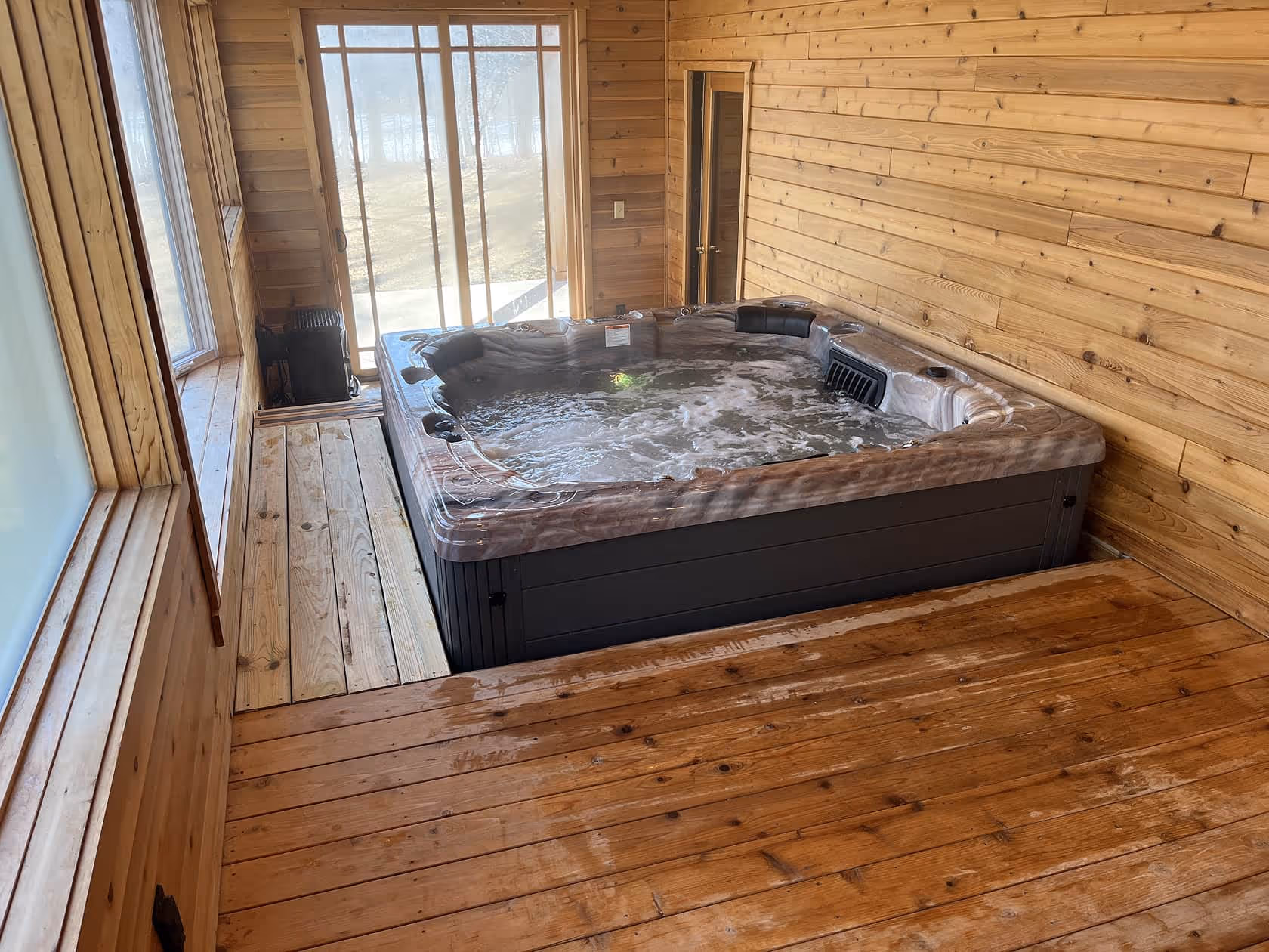 Large indoor hot tub set in a cedar-lined room with floor-to-ceiling windows and access to the outdoors.