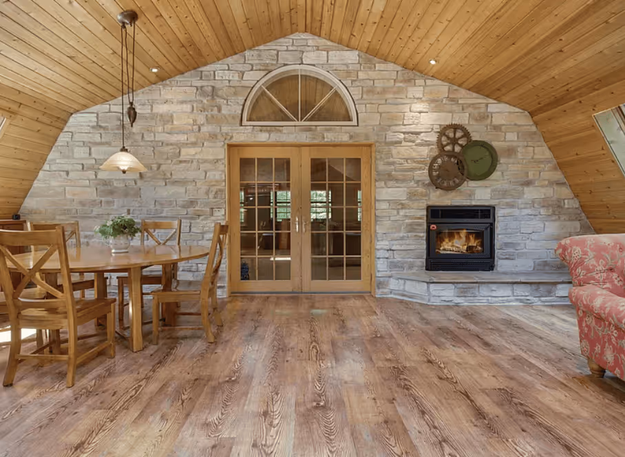 Dining space with wood floors, a stone fireplace, and French doors letting in natural light.