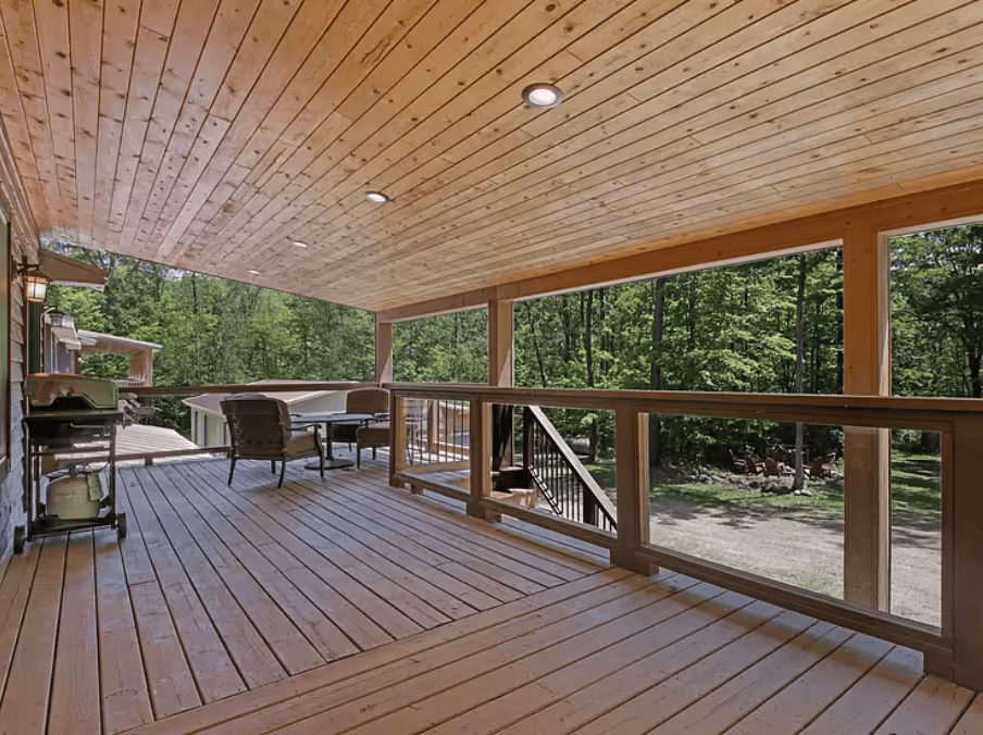 Large covered deck with a dining table and chairs, overlooking the surrounding forest.