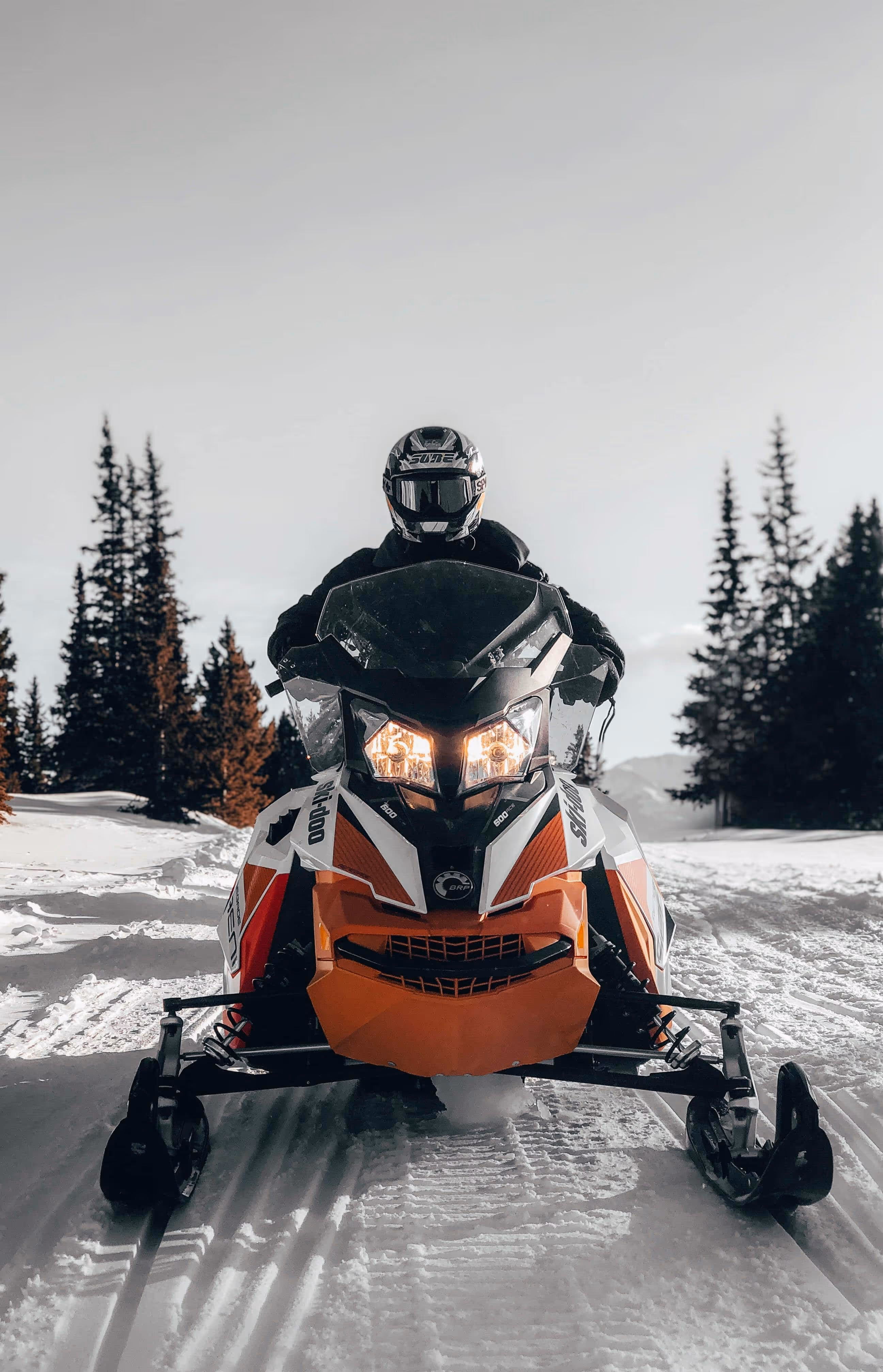Snow covered trail with a person with a helmet on an orange snowmobile