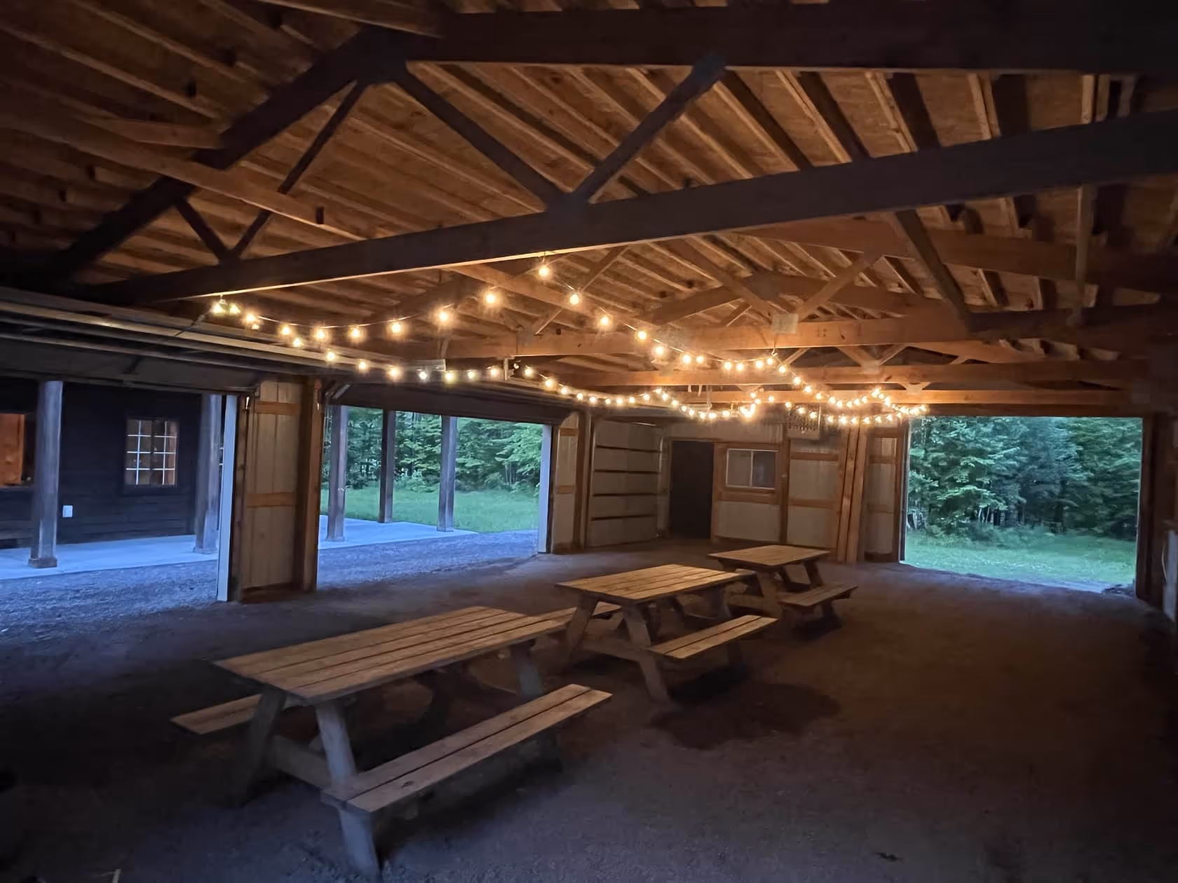 Rustic covered space with picnic tables and glowing string lights, perfect for group gatherings at Matson Lake Lodge.