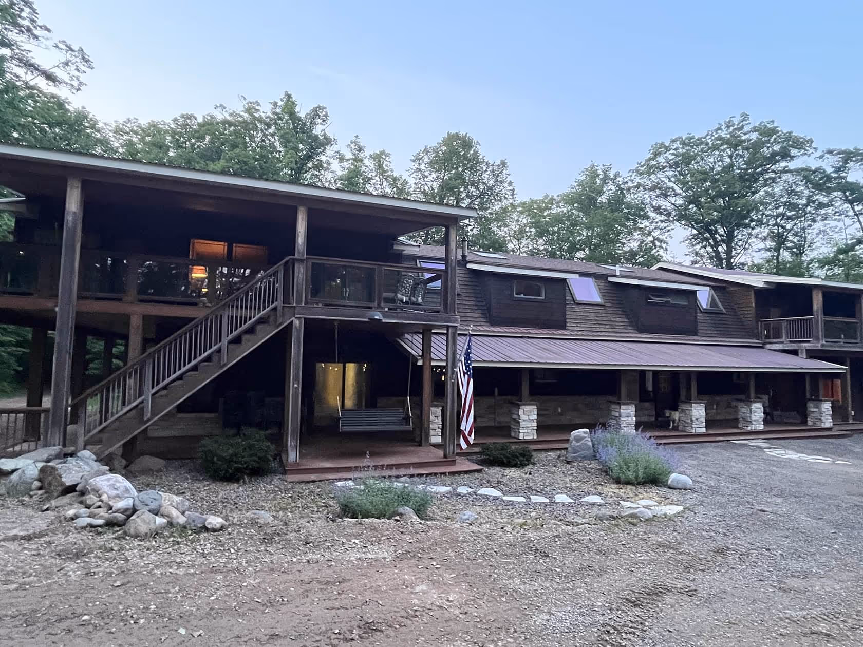 The rustic main lodge building with upper and lower porches, surrounded by trees and gravel paths.


