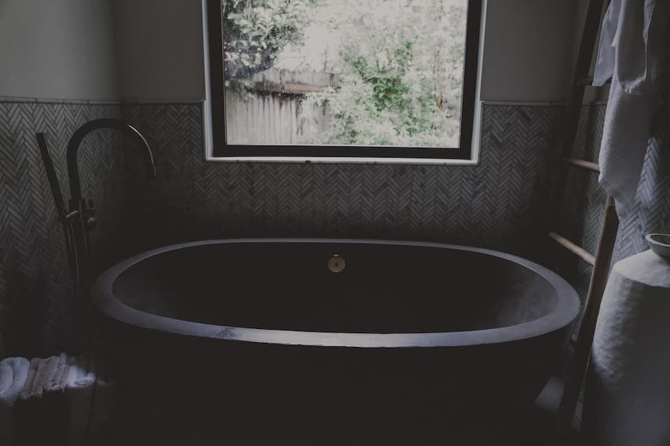 Dark bathtub under a window with a forest view.
