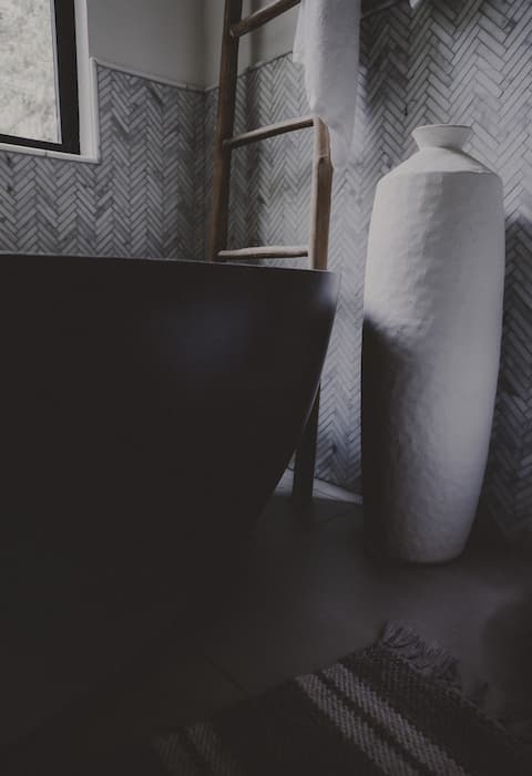 Matte black soaking tub with tall white vase nearby.