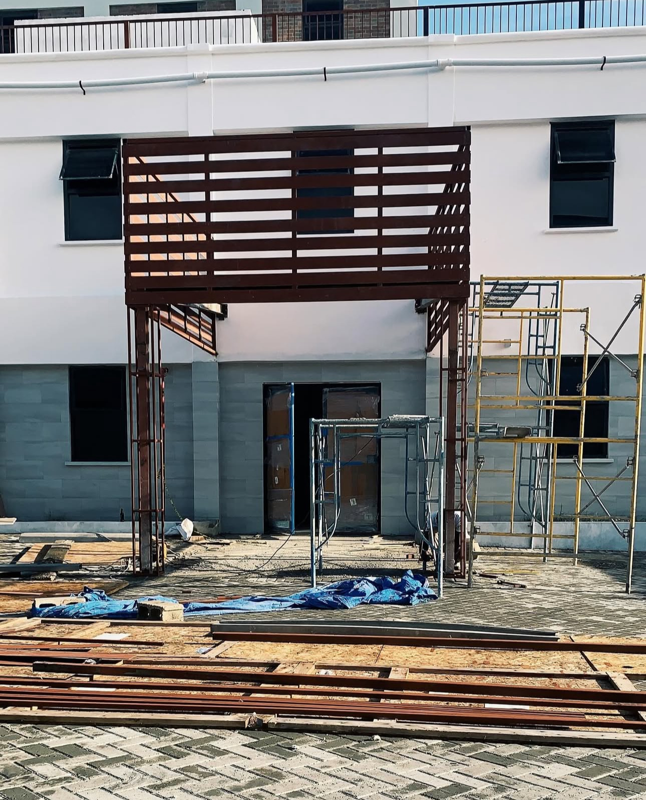 Construction site in front of a building with scaffolding, wooden planks, and a blue tarp on the ground.