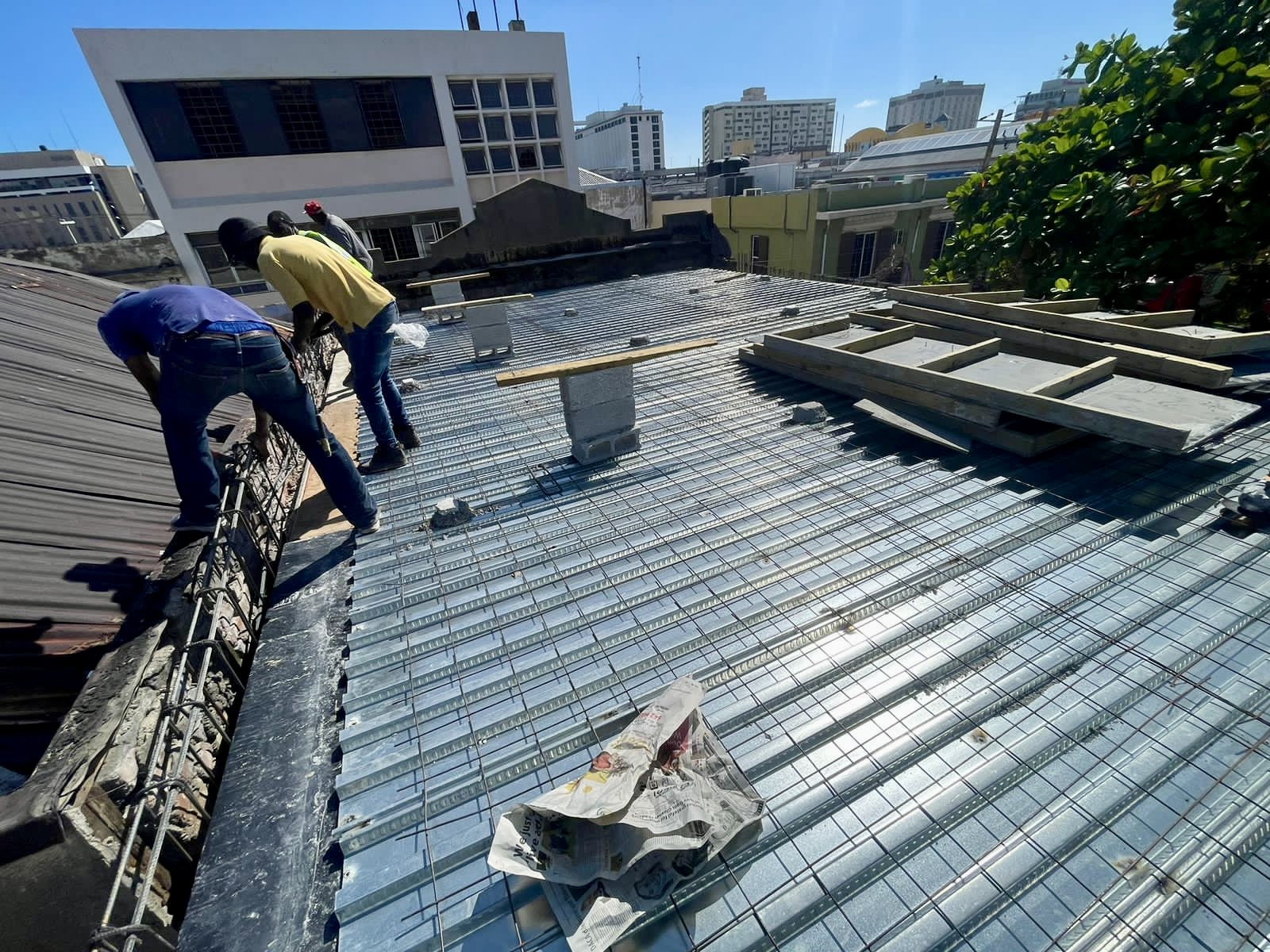 Three construction workers installing metal reinforcement on a building rooftop under clear blue sky.