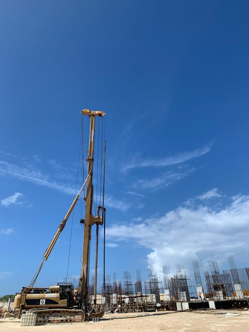 Construction site with a large drilling machine and partially built concrete structures under a clear blue sky.