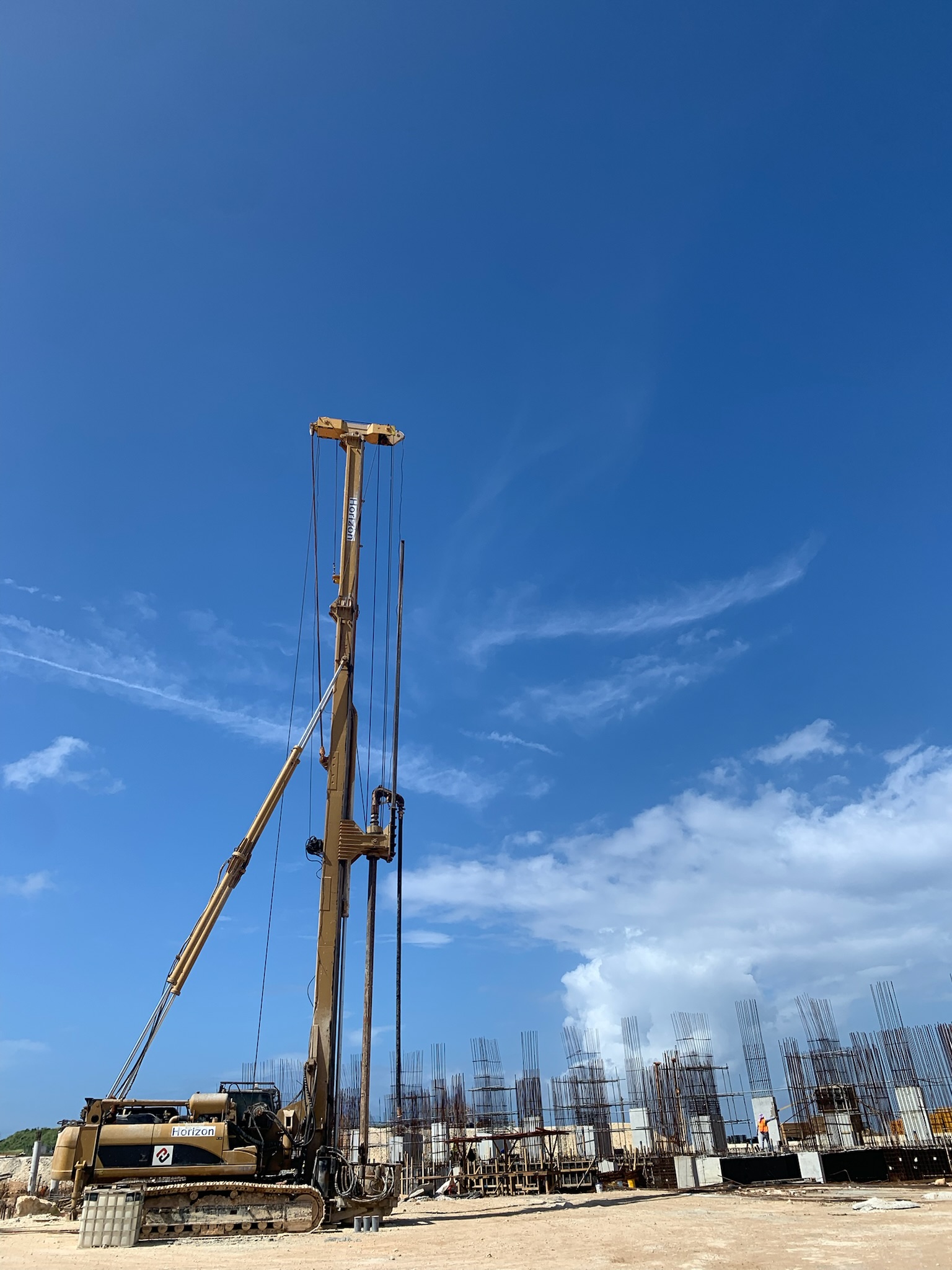 Construction site with a large drilling machine and partially built concrete structures under a clear blue sky.