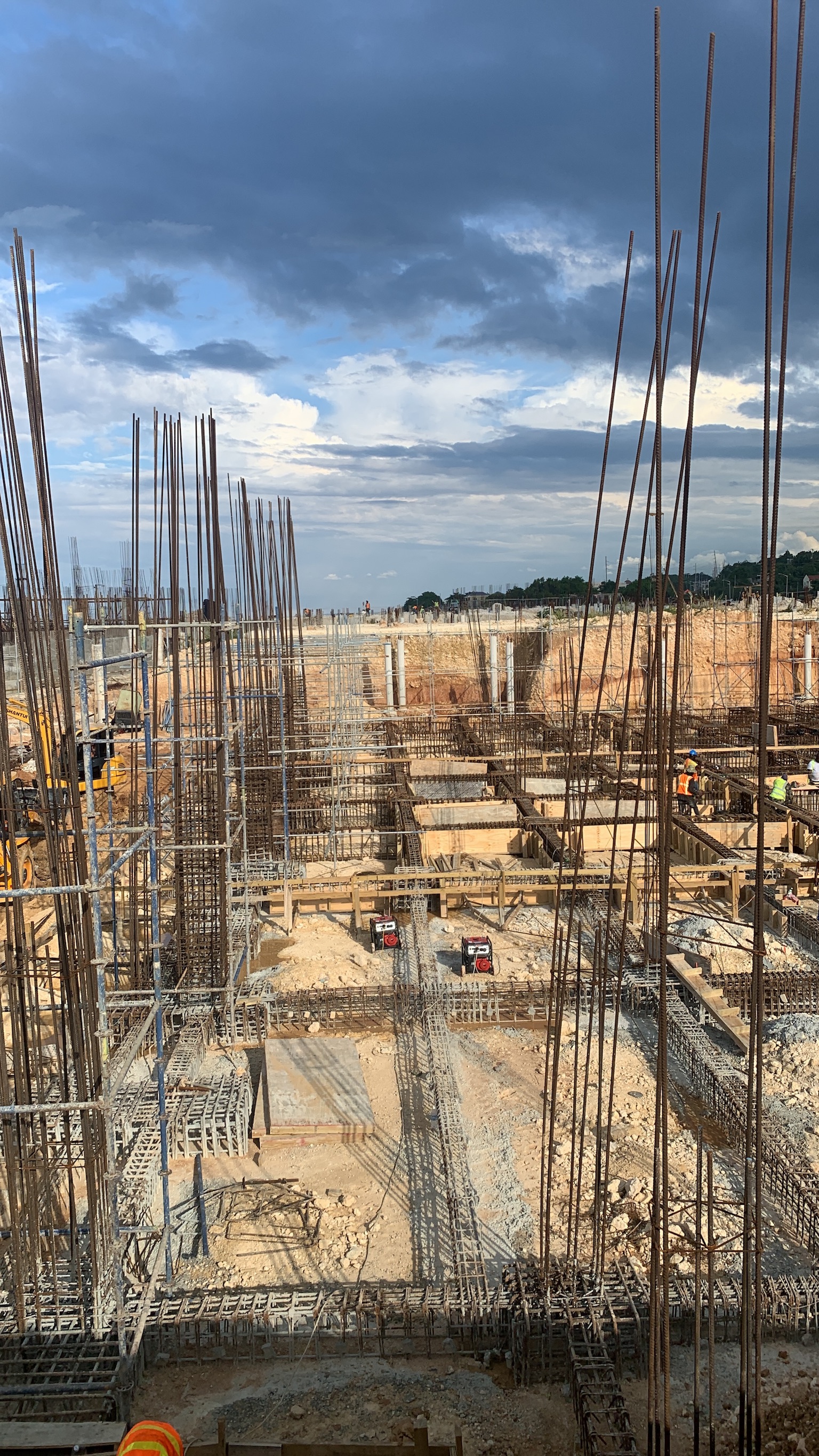 Construction site with steel reinforcement bars and workers under a partly cloudy sky.
