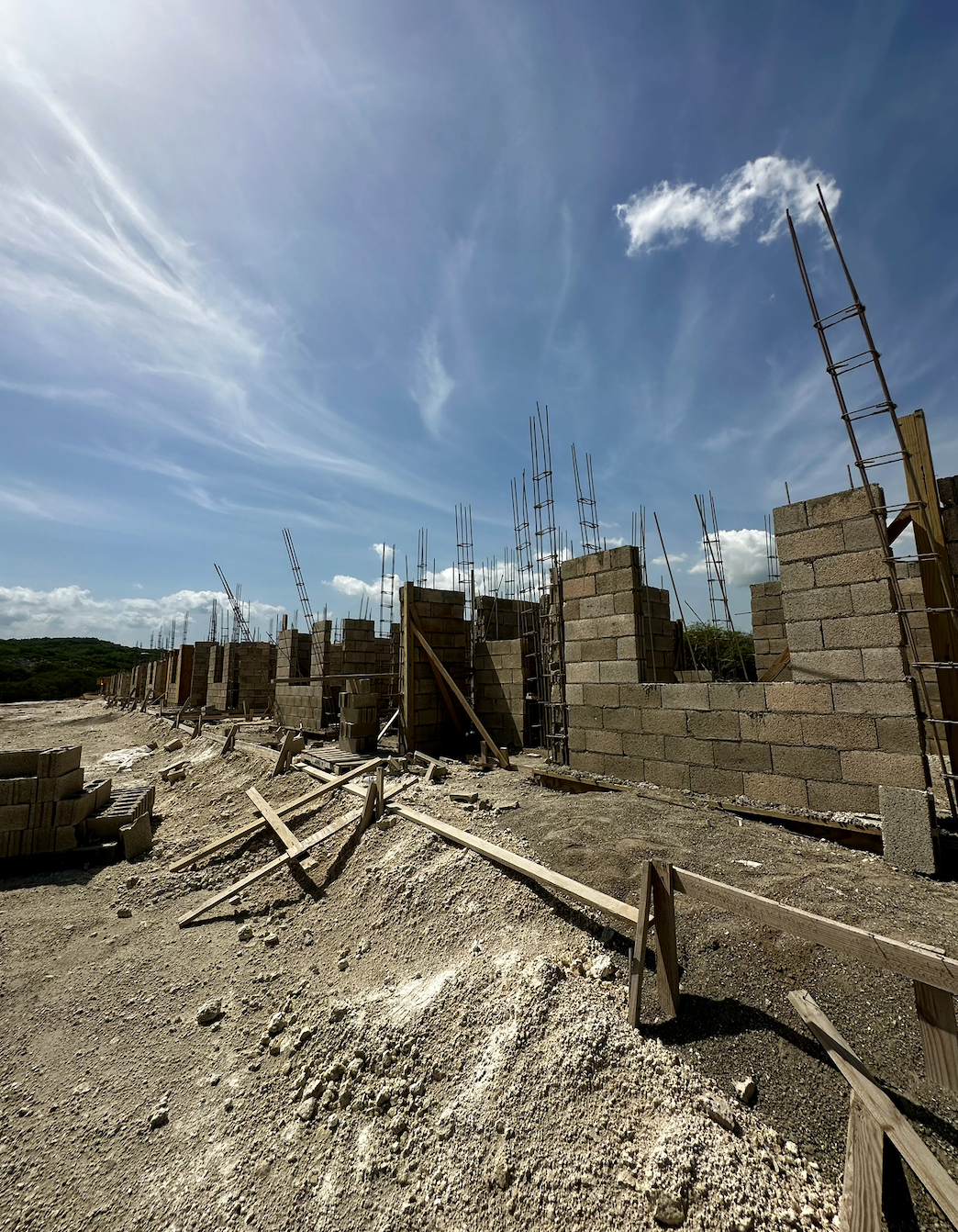 Construction site with partially built brick walls and steel rebar columns under a bright blue sky with wispy clouds.
