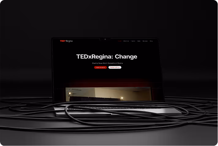 Laptop displaying TEDxRegina website with the headline 'TEDxRegina: Change' surrounded by black cables on a dark surface.