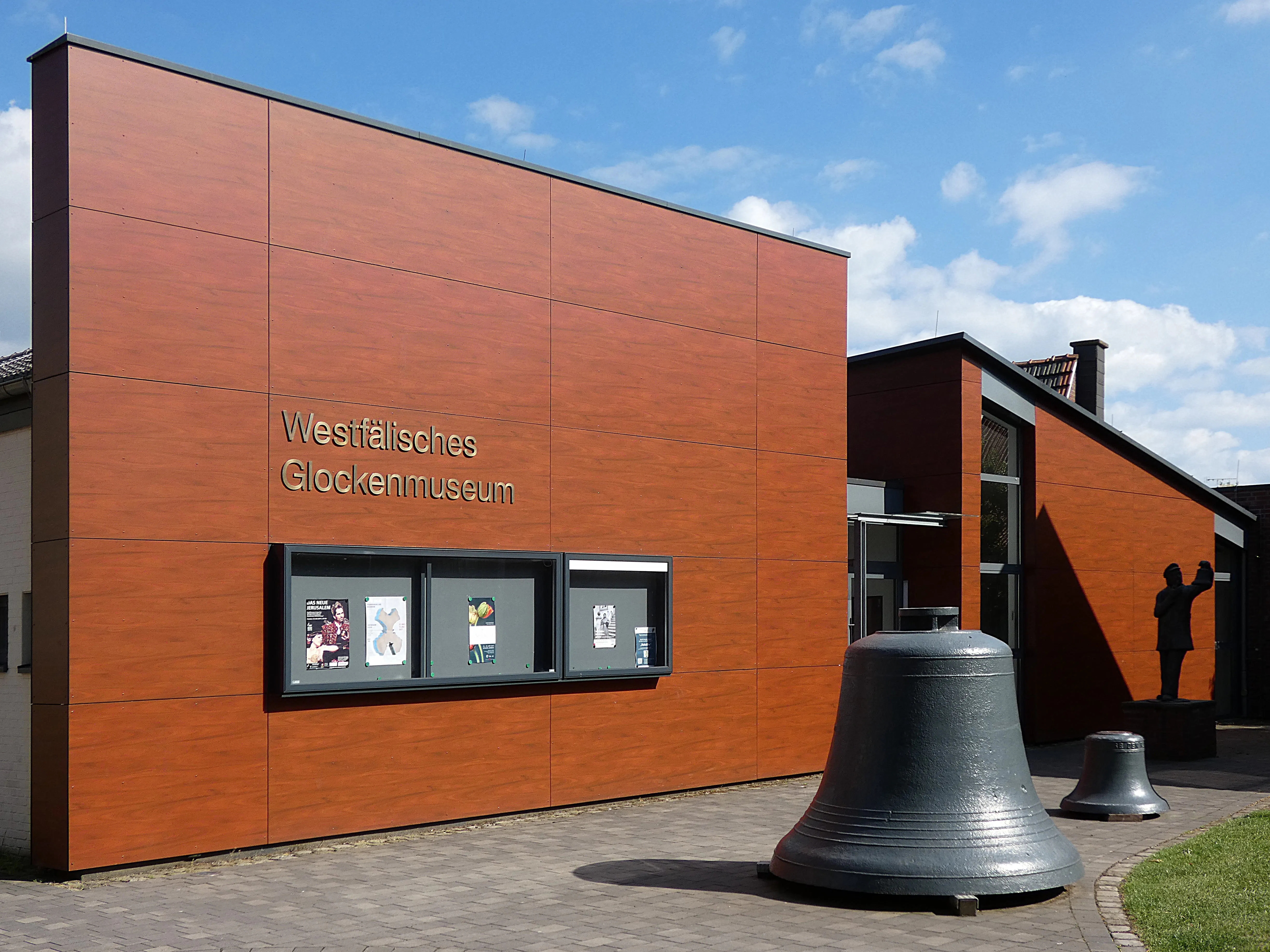 Westfälisches Glockenmuseum in Gescher – moderne Fassade mit Holzoptik, großen Glocken im Außenbereich und Statue im Hintergrund.