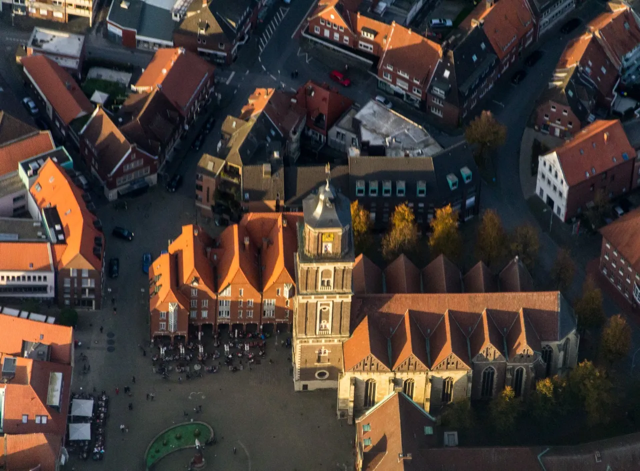 Luftaufnahme der St.-Lamberti-Kirche in Coesfeld mit historischem Marktplatz, umliegenden Gebäuden und roten Ziegeldächern.