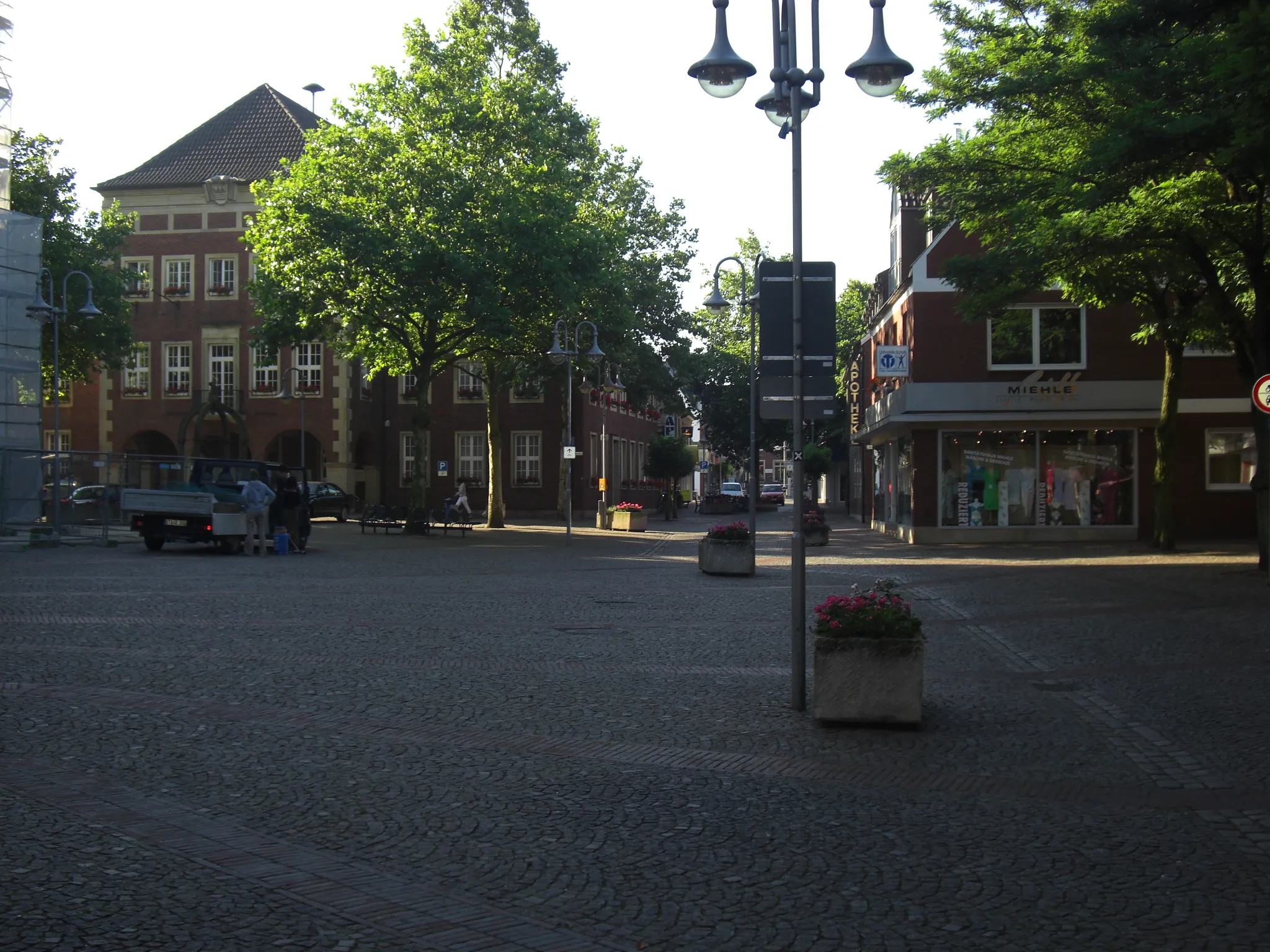 Blick auf den Marktplatz in Stadtlohn mit Kopfsteinpflaster, Blumenbeeten, Geschäften und historischen Backsteingebäuden im Abendlicht.