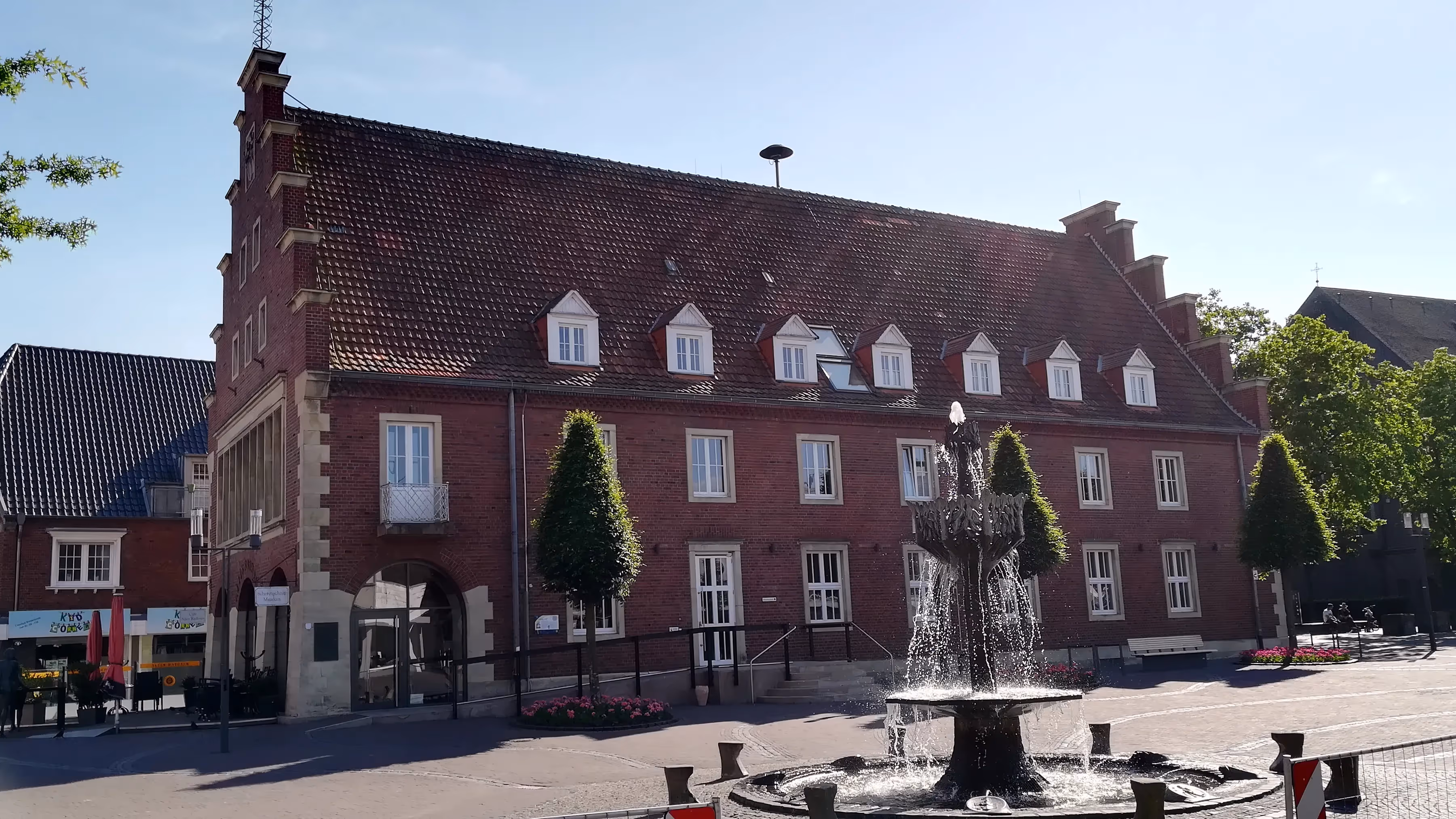 Historisches Rathaus von Vreden aus rotem Backstein mit Treppengiebel, zahlreichen Dachgauben und einem zentralen Springbrunnen im Vordergrund.