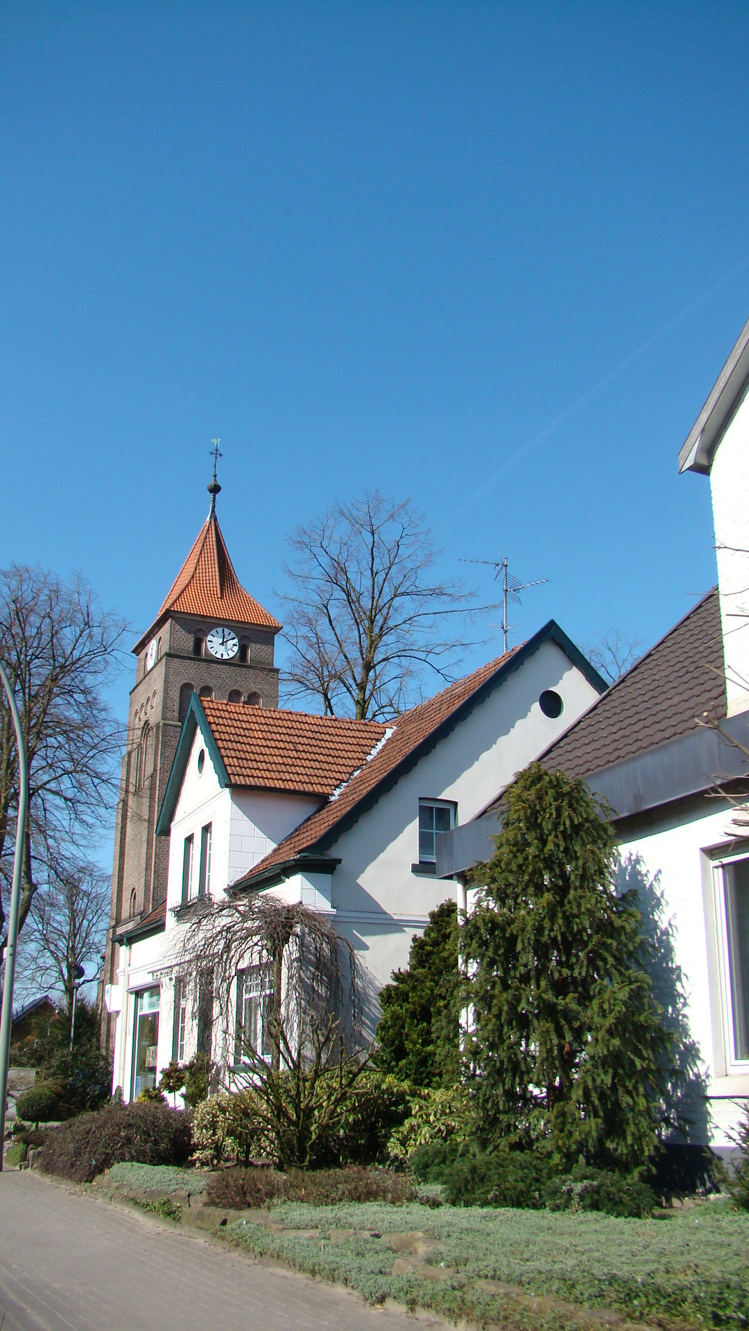 Evangelische Johanneskirche in Südlohn, weiß verputzter Bau mit hohen Spitzbogenfenstern und kleinem Glockenturm, umgeben von Bäumen und Grünflächen.