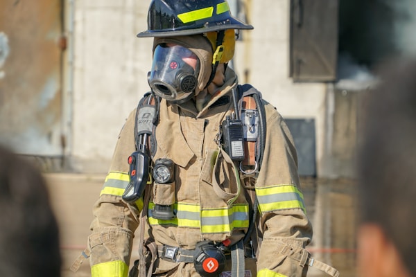 Firefighter wearing full gear helmet respirator mask and equipment helping to contain a warehouse fire.