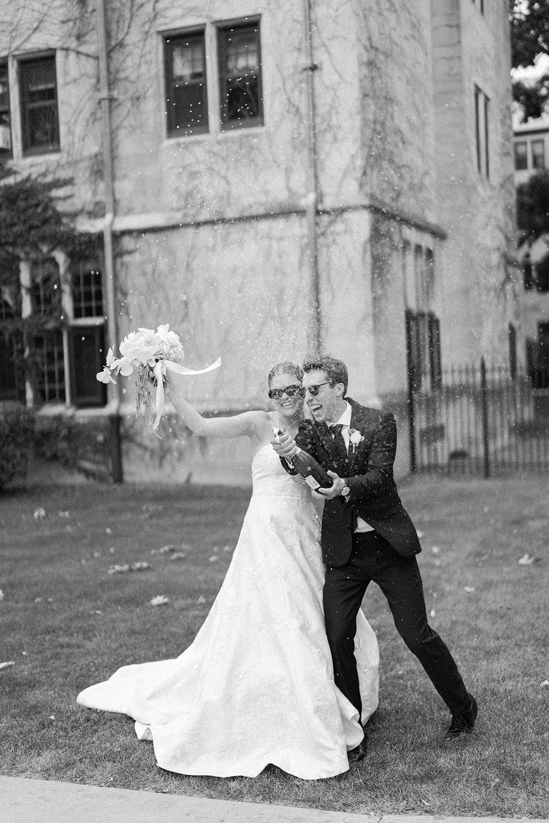 Couple joyfully popping a bottle of champagne, celebrating with laughter and excitement during their wedding day.
