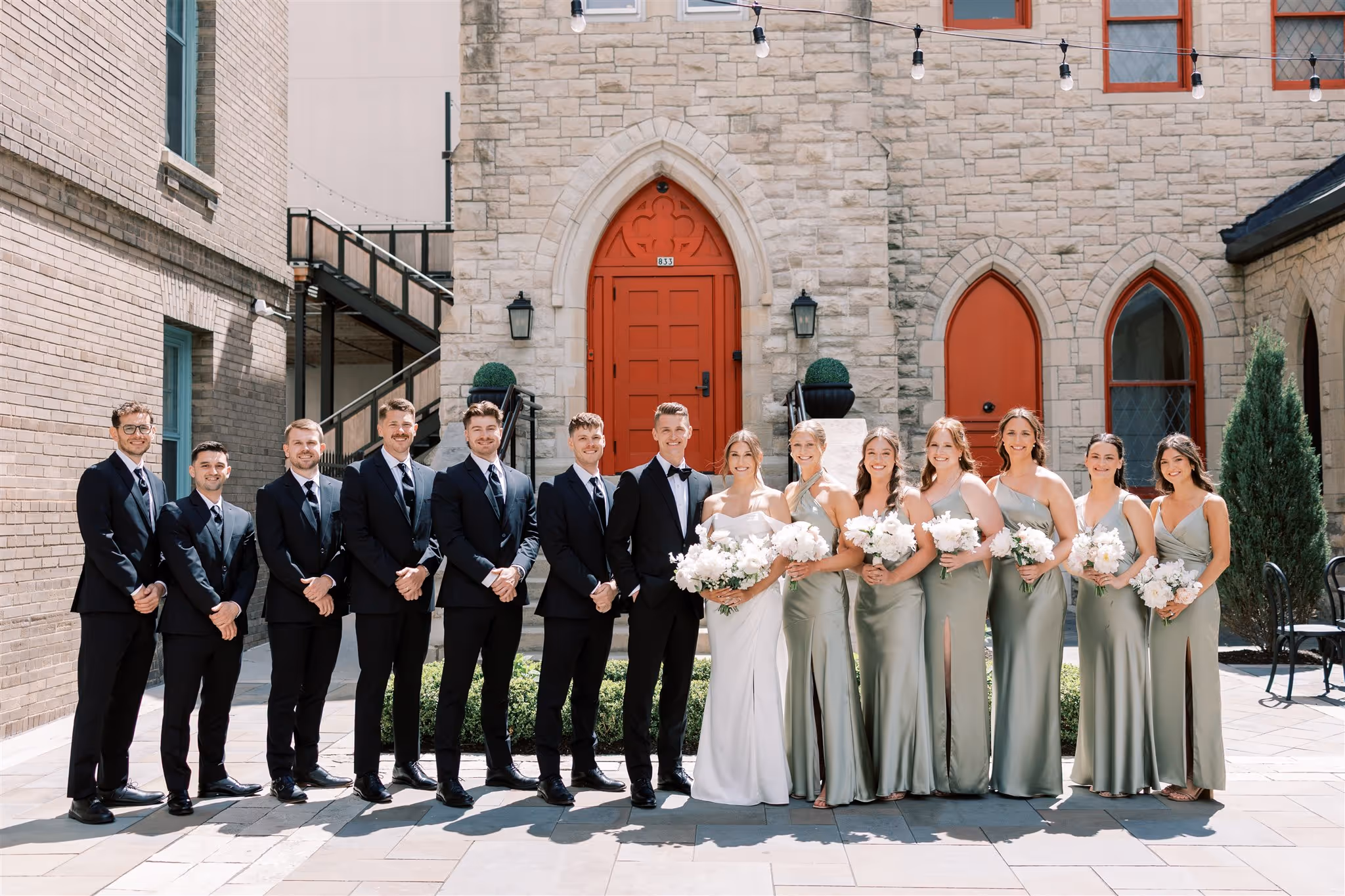 Wedding party smiling and standing together in front of a church before the ceremony.