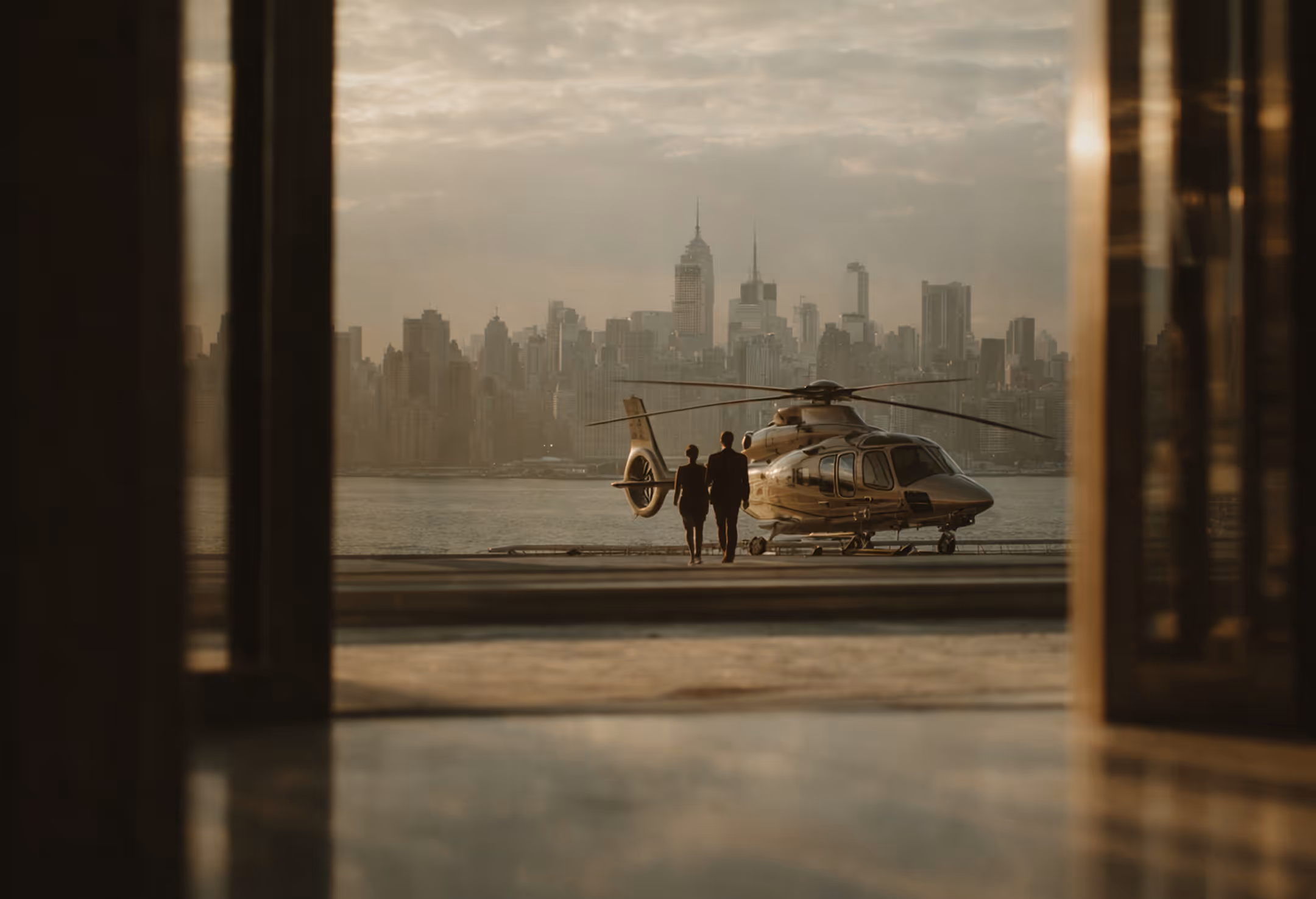 Two people walking toward a helicopter parked near a waterfront with a city skyline in the background.