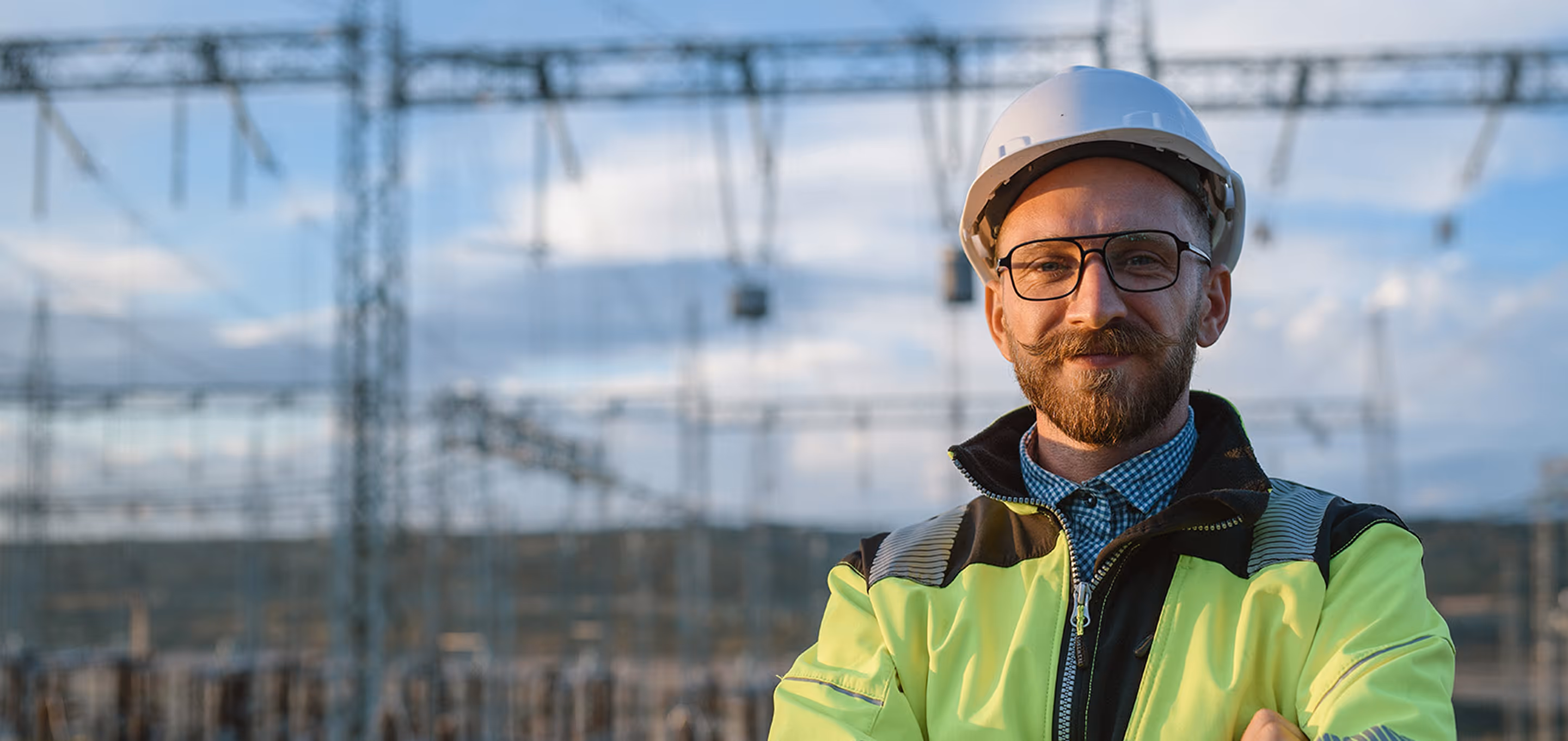 Man in safety gear and hard hat standing outdoors, smiling confidently.